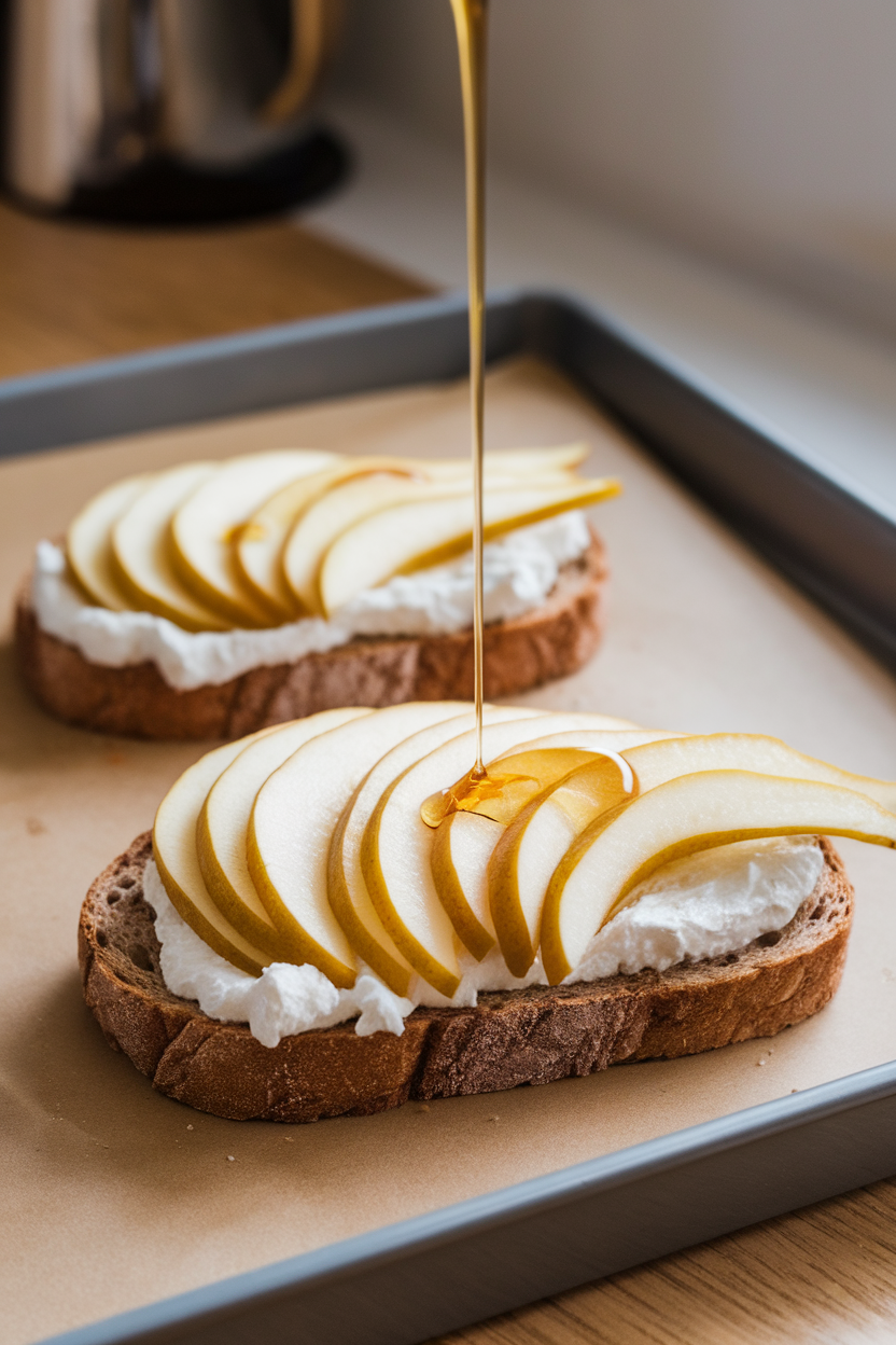 Photo of whole-grain toast spread with ricotta, fanned pear slices, and a light drizzle of honey, set on an indoor breakfast tray. No text or logos anywhere.