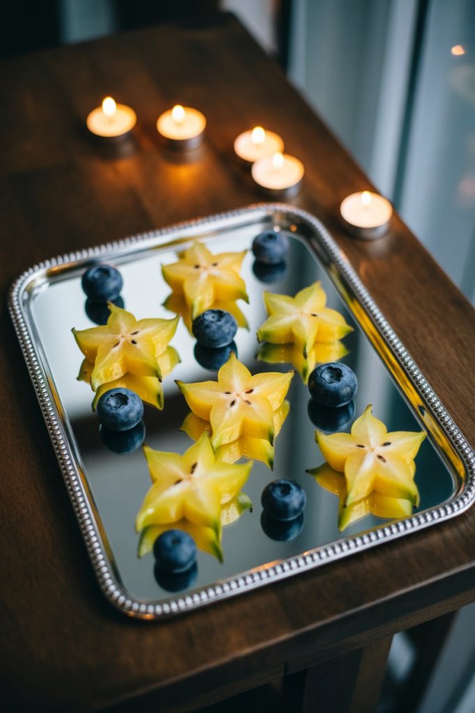 A mirrored tray indoors with luminous yellow starfruit slices scattered amongst blueberries, lit by dim candlelight. No text or logos.