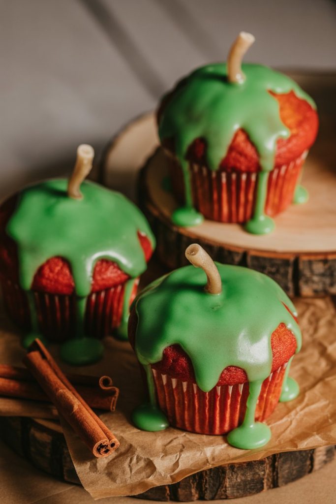 Photo of red apple-spice cupcakes with glossy green candy glaze dripping over the top, indoor lighting, no text or logos.