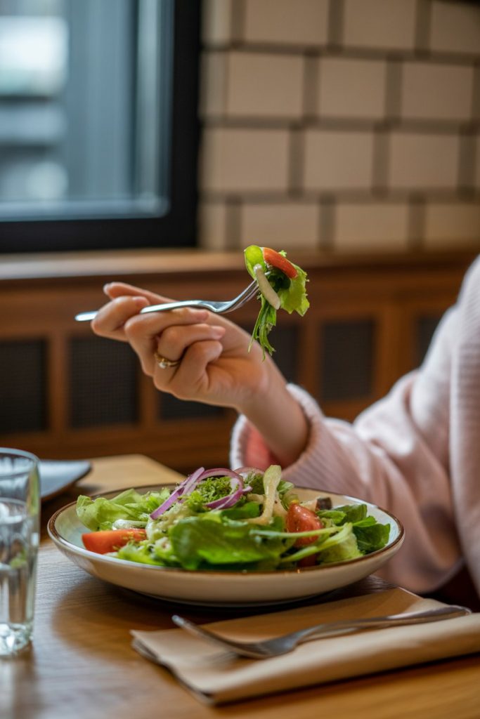 An indoor dining nook with a person holding a forkful of salad, eyes on the plate rather than a phone—photo, no visible faces or logos.