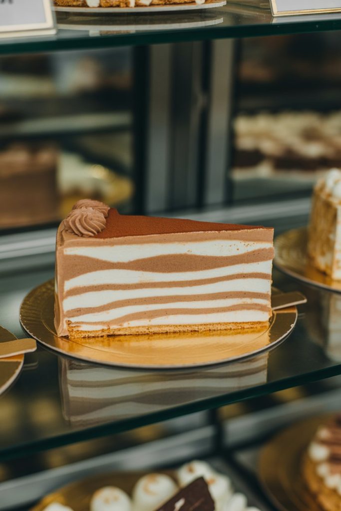 An indoor patisserie case displaying a slice of almond meringue layers alternating with mocha buttercream. No text or logos. Photo, not illustration.