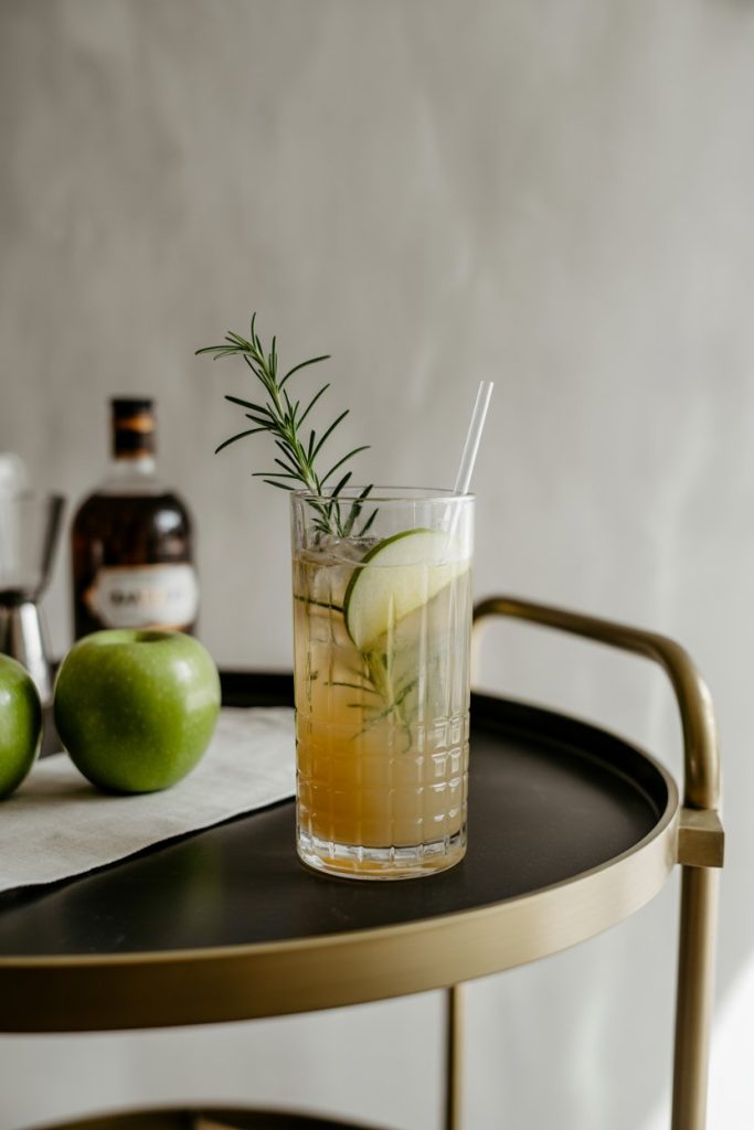 Indoor bar cart with a tall Collins glass of apple rosemary collins, clear straw, sprig of rosemary standing tall. Photo, no text or logos.