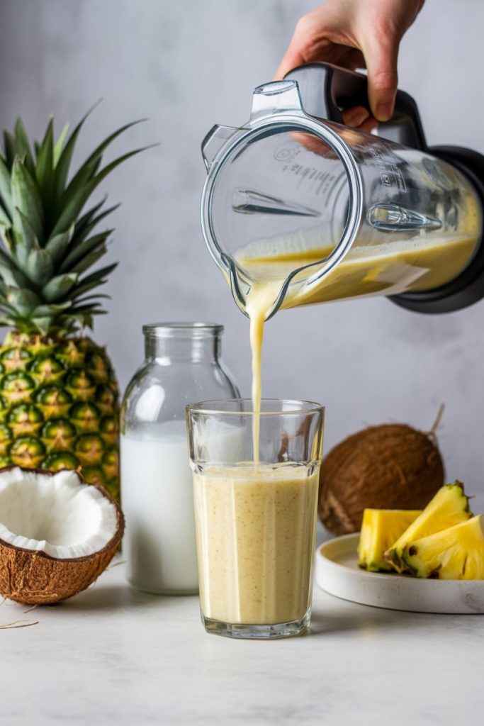 Indoor countertop Blender jar pouring a tropical smoothie into a glass, ingredients like pineapple and coconut water nearby; no text or logos, photo style.