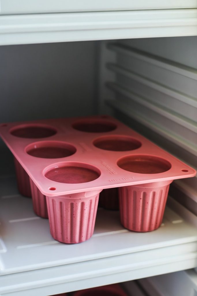 Silicone mold filled with berry smoothie mixture on a freezer shelf, indoor photo, no text or logos