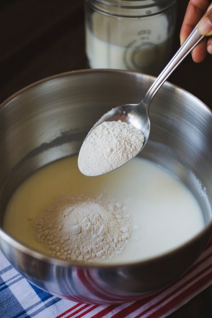 Spoon scooping powdered milk into a mixing bowl, indoor photo, no text or logos