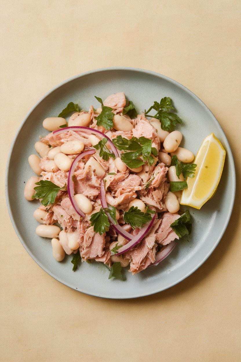 An indoor lunch plate with flaked tuna, cannellini beans, red onion slivers, and parsley tossed lightly, photo, no text or logos.