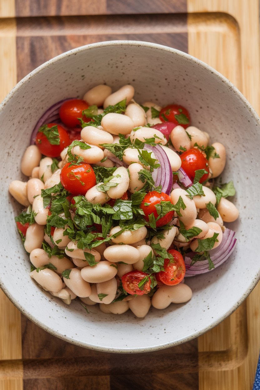 Indoor photo of cannellini beans tossed with chopped parsley, cherry tomatoes, and red onion in a serving bowl. No text or logos; photograph.
