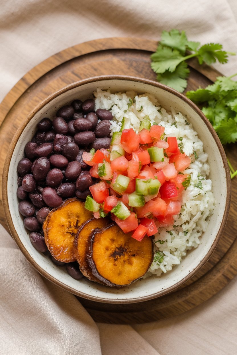 Indoor scene of a shallow bowl filled with black beans, caramelized plantain rounds, cilantro rice, and pico de gallo. No text or logos present.
