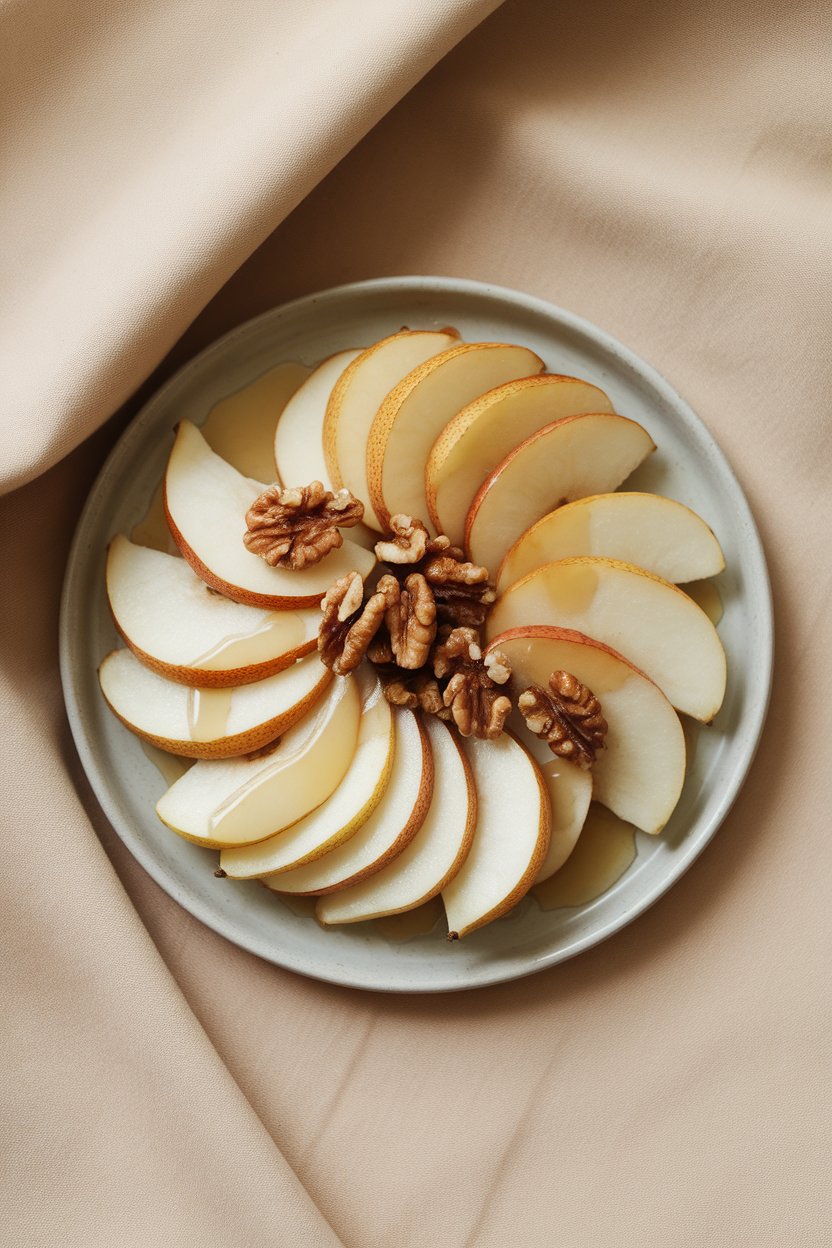 Indoor photo of sliced pears arranged with toasted walnuts and a light maple drizzle on a dessert plate. No text or logos.