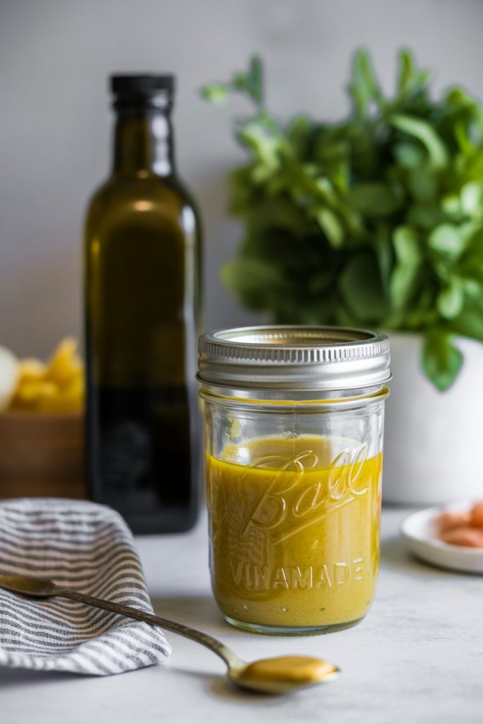 Indoor countertop featuring a mason jar of homemade vinaigrette, olive oil bottle, and mustard spoon—photo.