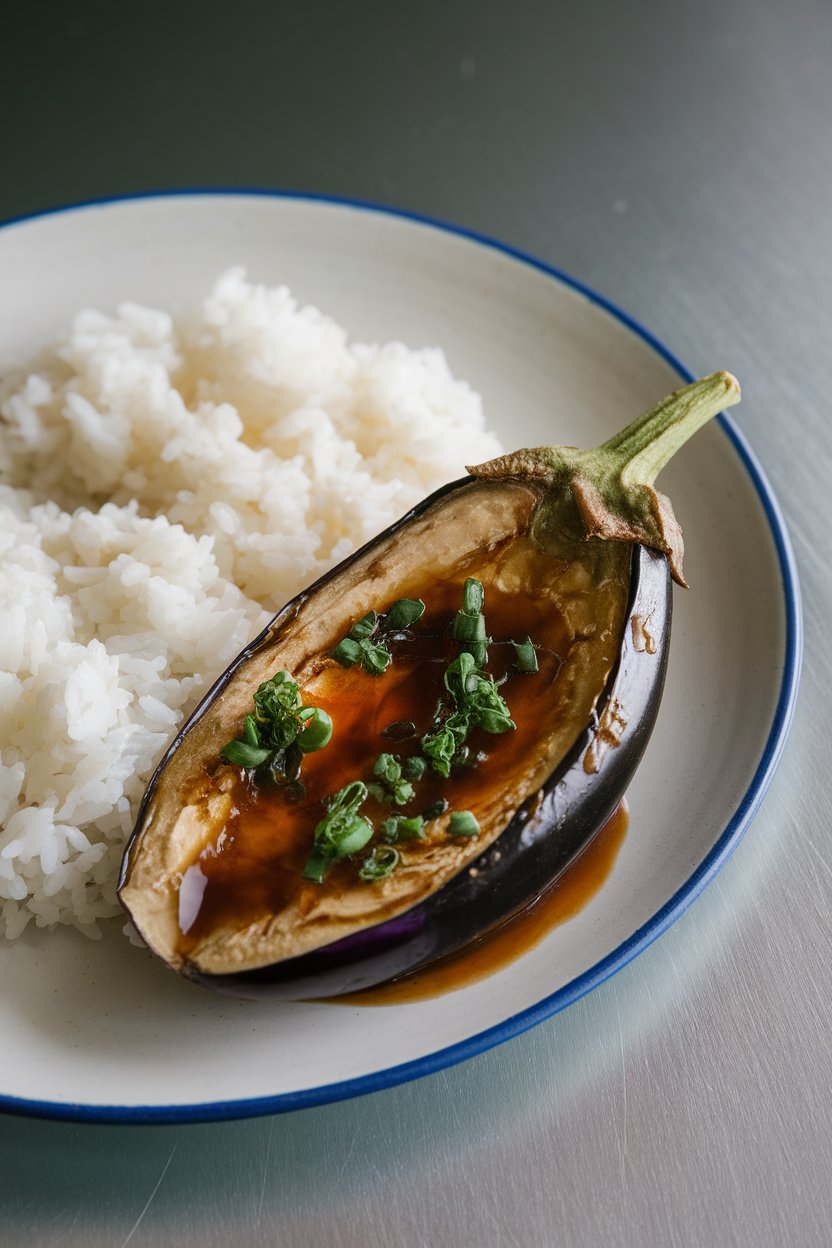 Indoor dinner plate featuring halved eggplants glazed with caramelized miso sauce, steamed white rice alongside. No text or logos. Photo, not illustration.
